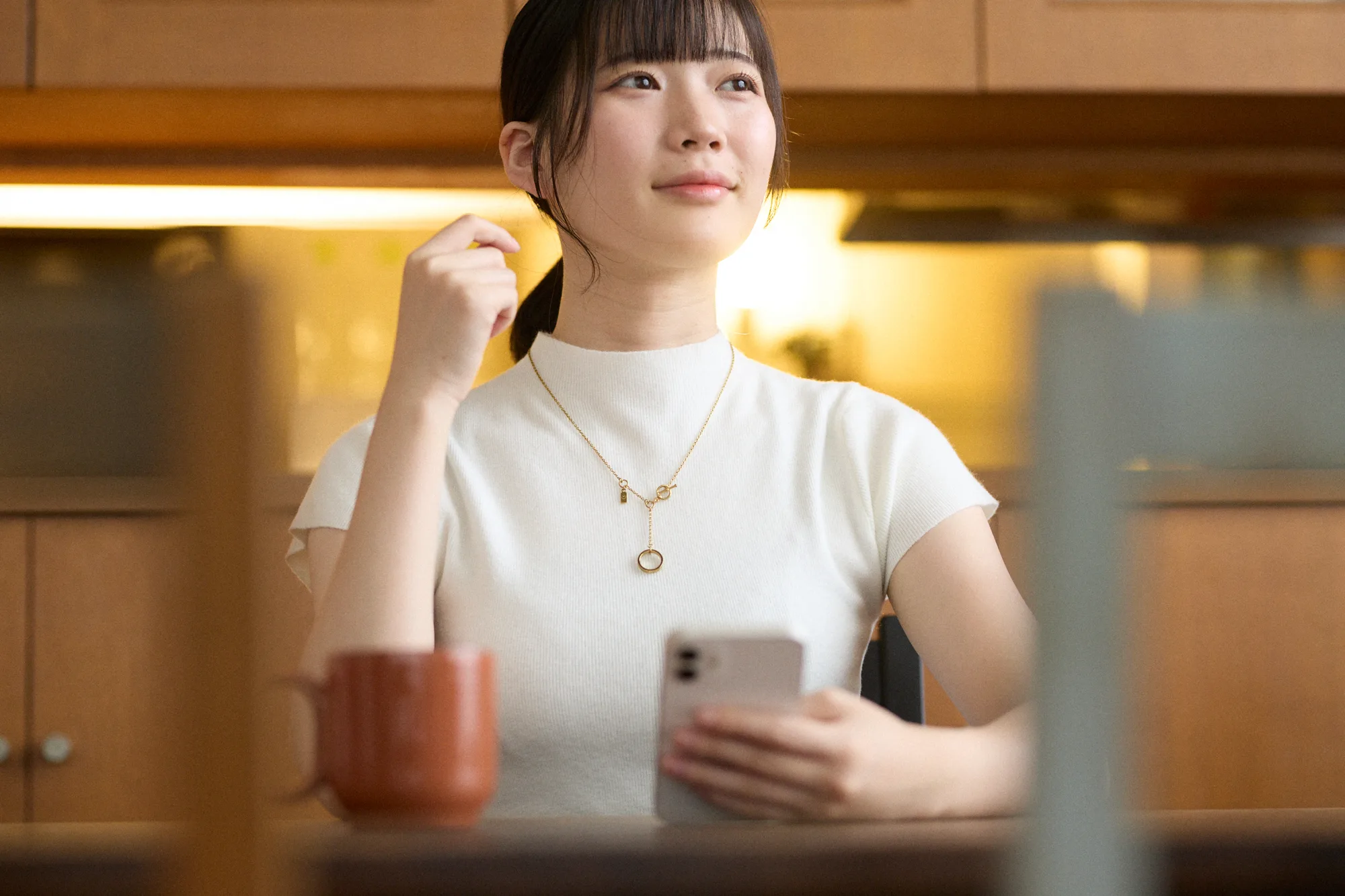 白いニットにゴールドのネックレスを着け、カフェでくつろぐ女性